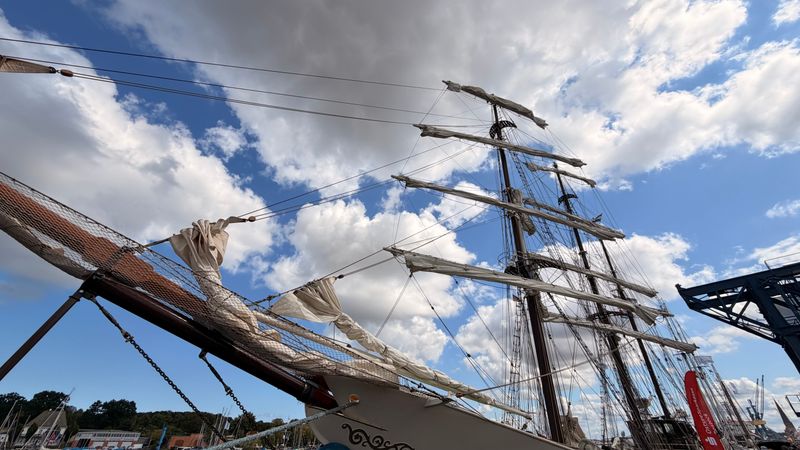 Majestic tall ship with ornate rigging against a bright blue sky at a festival dock
