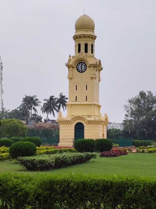 Free Yellow clock tower set amidst lush green gardens, charming and serene vibe. Stock Photo