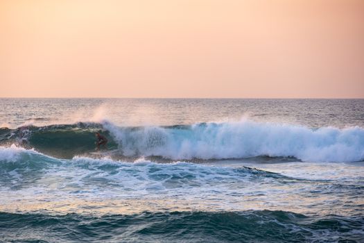 A surfer skillfully rides a wave during a stunning sunset over the ocean, capturing the thrill of the sport.