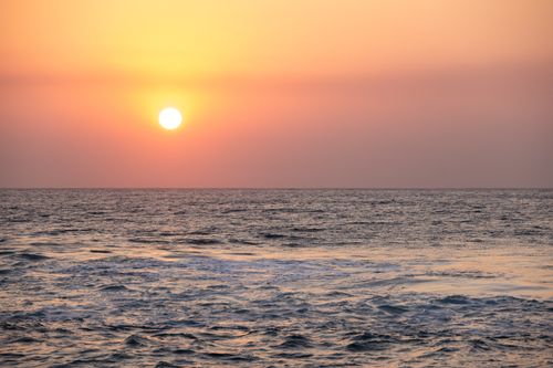 Free Serene sunset over the ocean with soft hues of orange and pink reflecting on the calm sea waves. Stock Photo