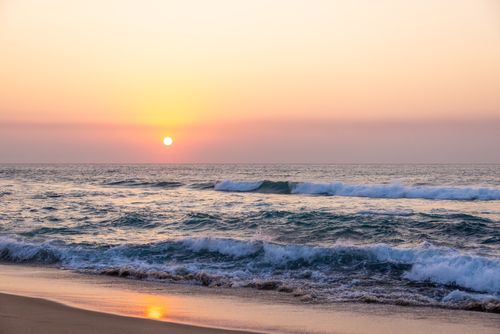 Free A peaceful sunset over gentle ocean waves on a sandy beach, evoking tranquility and nature's beauty. Stock Photo