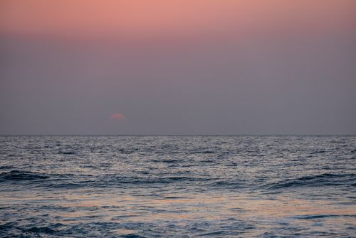Free A tranquil scene of the sun setting over a calm ocean, filling the sky with soft pastel colors. Stock Photo