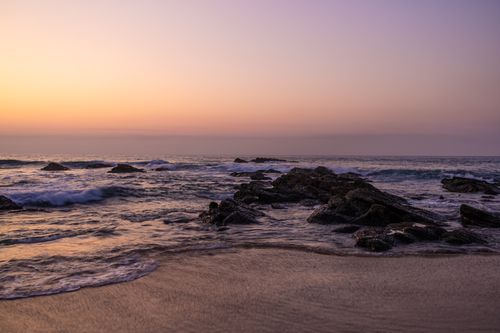 Free A tranquil scene of rocky shoreline with waves and a vibrant sunset sky over the ocean. Stock Photo