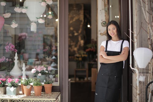  Woman in White Crew neck T-shirt Wearing Black Apron Leaning on Glass Door