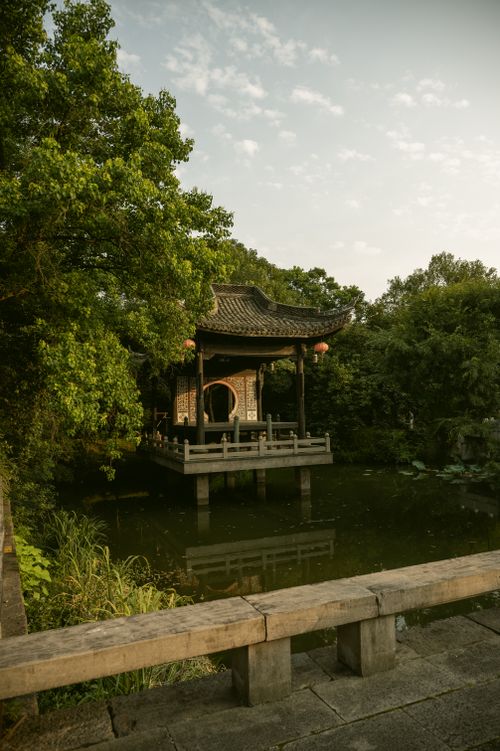 Free Traditional Asian pavilion by a peaceful pond surrounded by lush greenery at daytime. Stock Photo