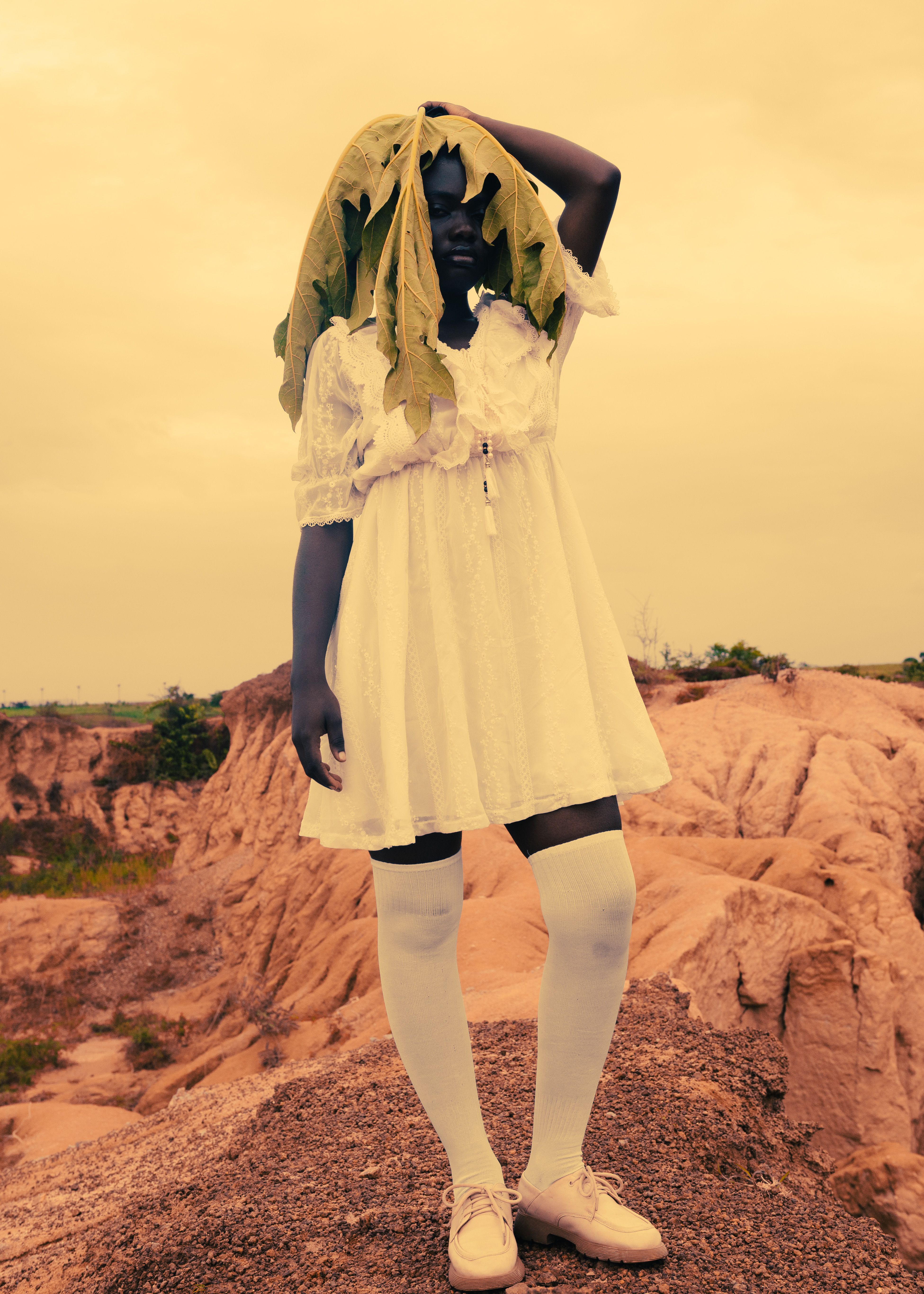 A warm-toned portrait featuring an individual in a white dress standing in a rocky outdoor setting.