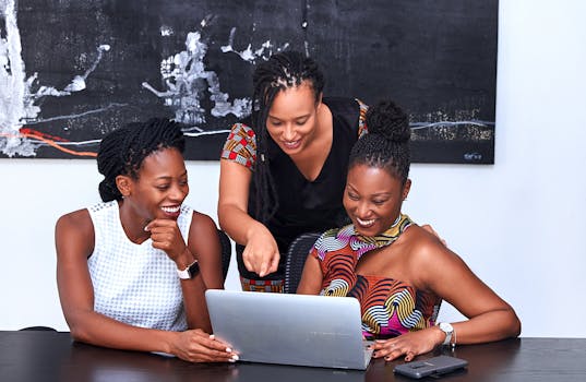 Three African American women collaborating at a laptop, focused and happy during a meeting indoors.