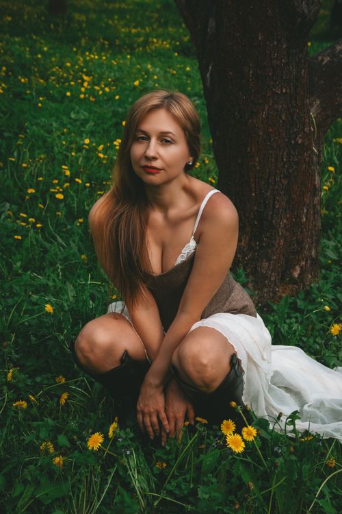 Free A woman kneels gracefully among blooming dandelions in a serene forest setting. Stock Photo