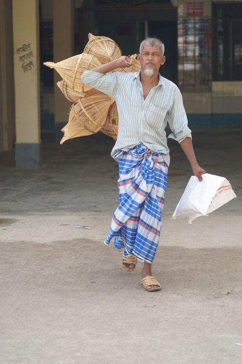 Free A Bangladeshi man carrying traditional woven baskets in a village setting. Stock Photo