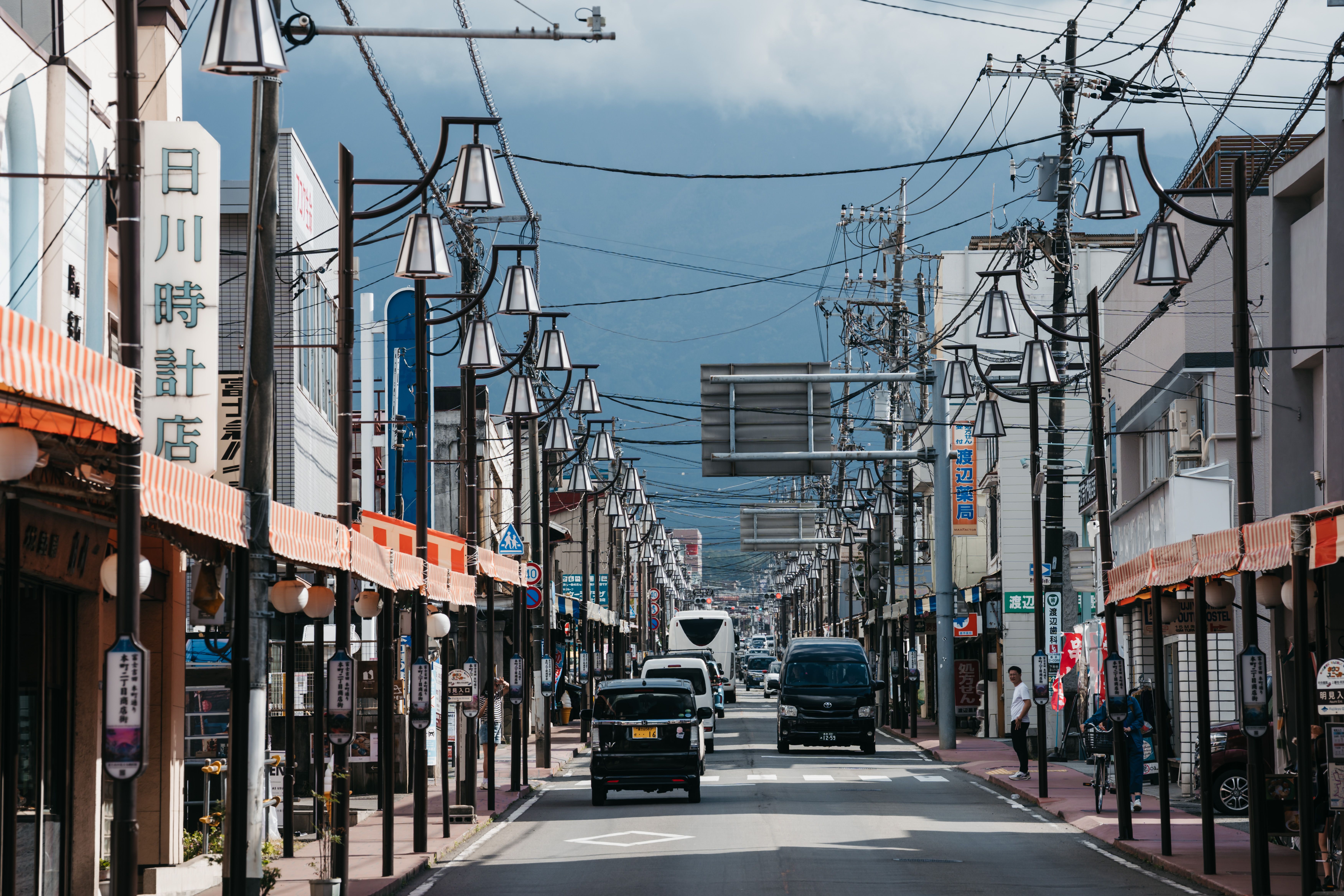 商店や交通量の多い活気ある日本の街並みと、背景にそびえる山々。
