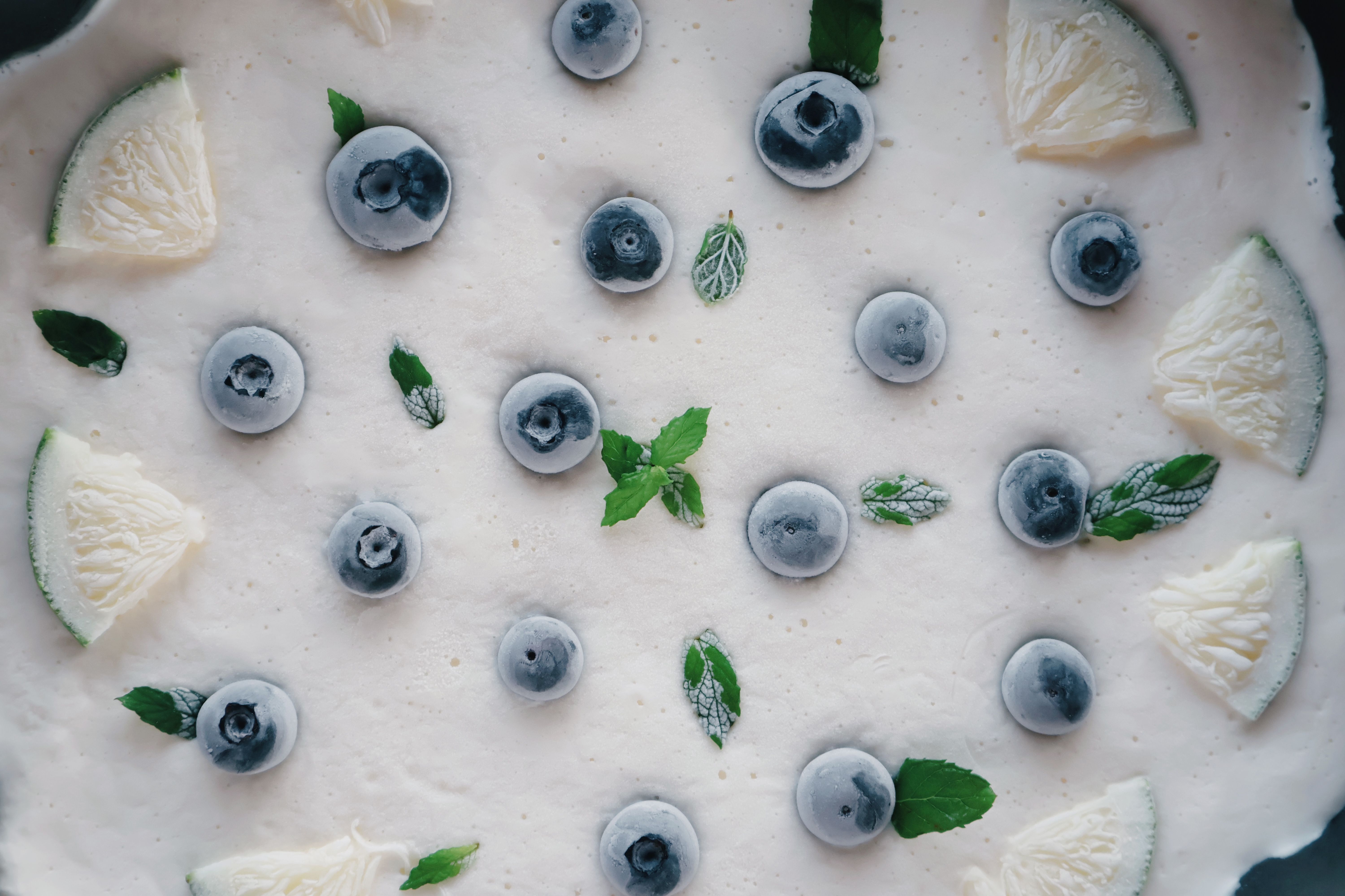 Flat lay of frozen blueberries and lime slices on a creamy dessert surface with mint leaves.