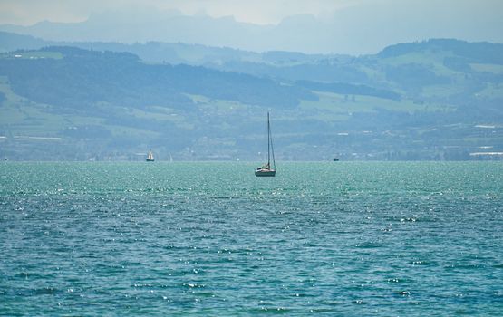 Serene view of sailboats on a tranquil lake with majestic mountains in the background.