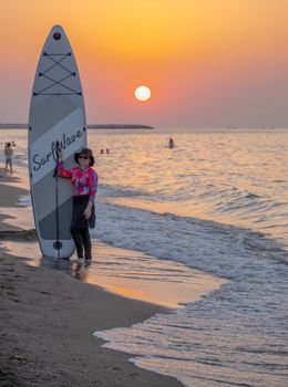 A woman in a wetsuit stands by her paddleboard on a beach during a stunning sunset in Karacabey, Bursa, Türkiye.