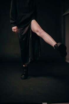 Stylish woman in dark attire and boots captured with a moody aesthetic on a black background.
