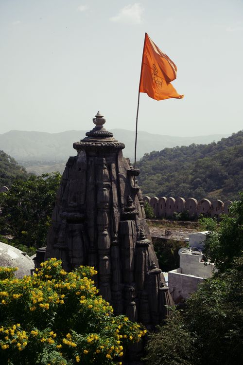 Free Ancient temple in Rajasthan with a vibrant orange flag amid green hills and clear skies. Stock Photo
