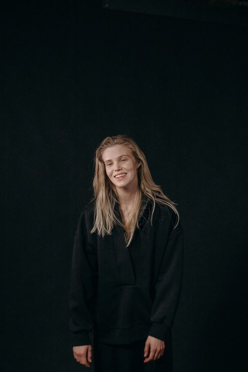 Free Portrait of a smiling woman with blond hair in dark clothing, captured against a black background. Stock Photo