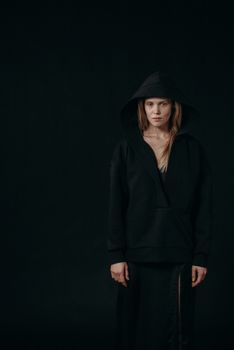 A striking portrait of a woman in a black hoodie against a dark background.