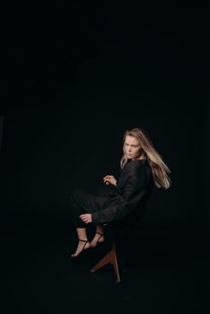 Elegant blond woman posing on a stool with a dark background in a studio setting.