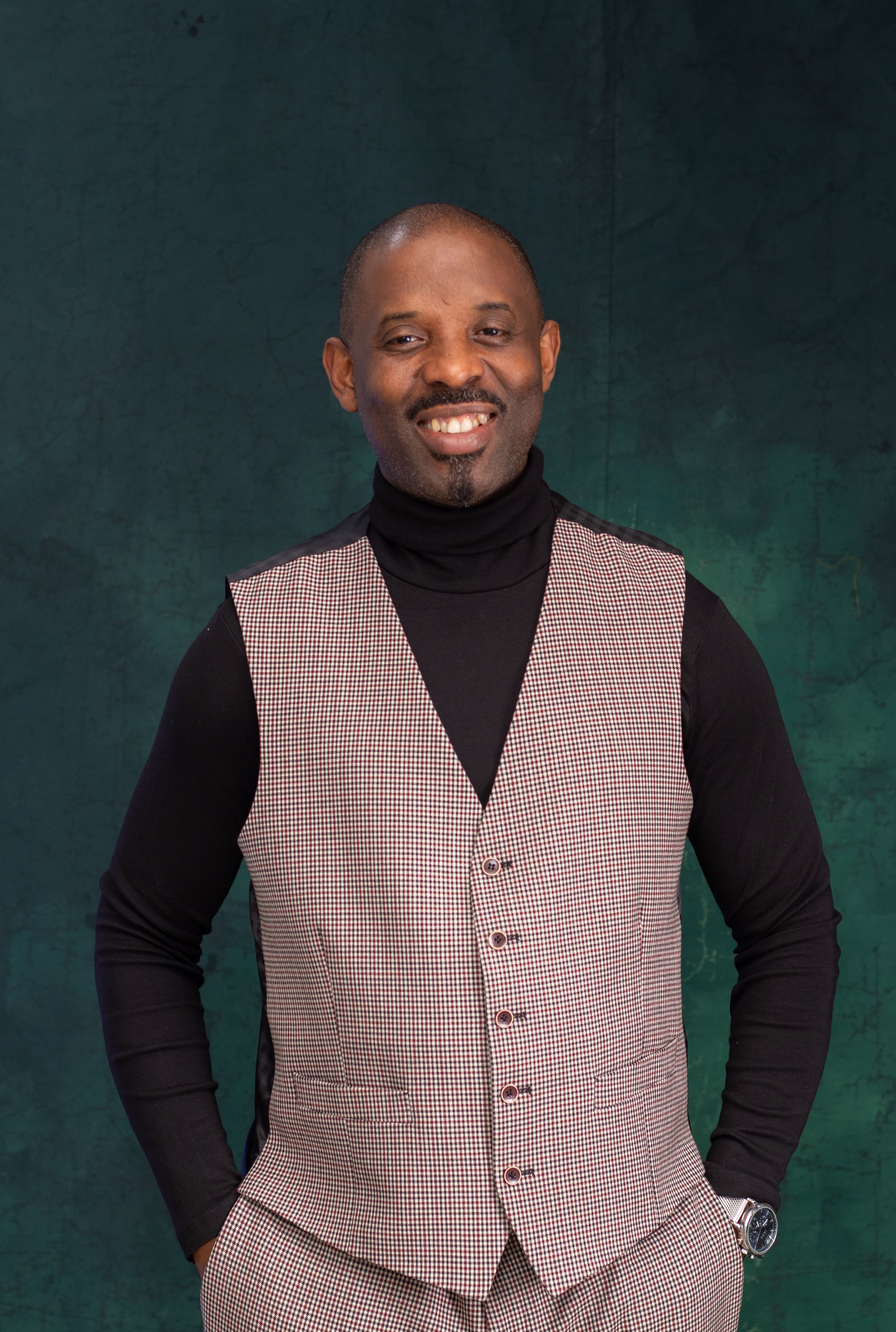 A cheerful man poses confidently in a checkered vest against a green textured backdrop.
