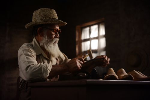 Free Senior artisan working on leather shoes in dimly lit workshop, showcasing traditional craftsmanship. Stock Photo