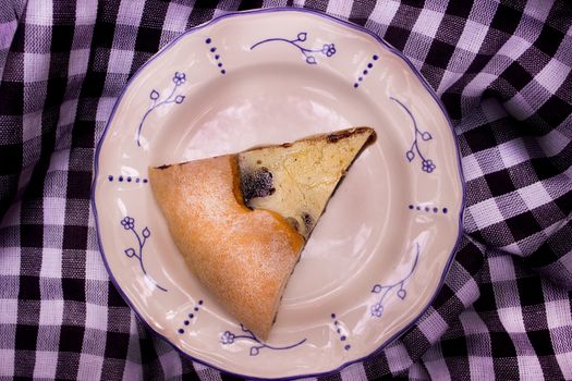 A single slice of traditional Belgian pastry on a floral-decorated plate atop a checkered cloth.