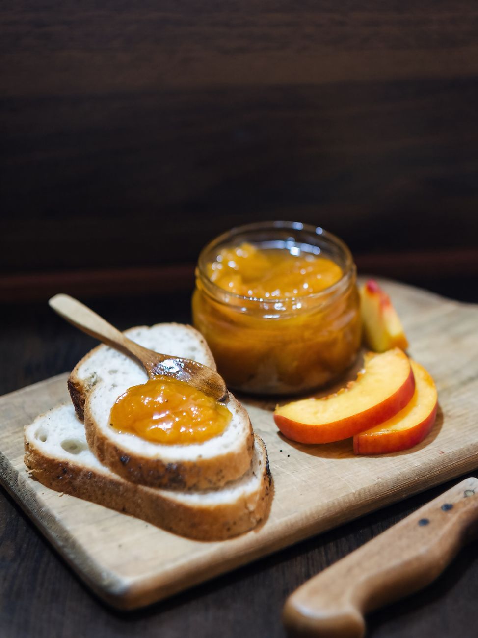 Sliced bread topped with delicious homemade peach jam on a wooden board with peach slices.