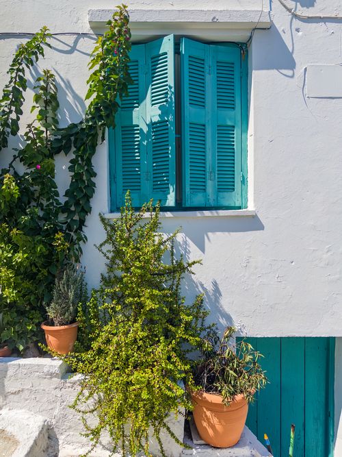 Free Whitewashed wall with vibrant blue shutters and potted plants in Greece. Stock Photo