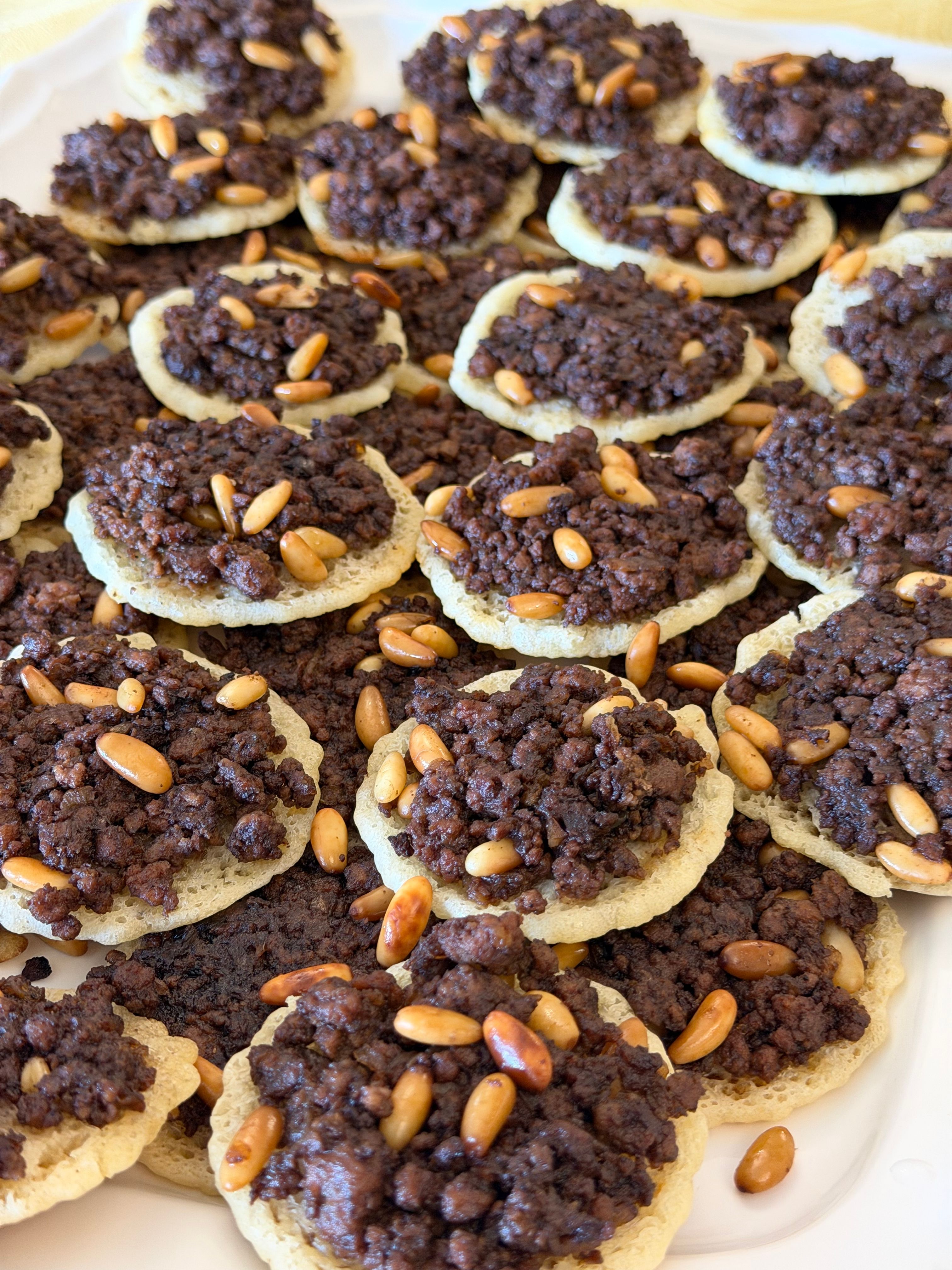 Close-up of Lebanese sfiha topped with seasoned meat and pine nuts on a platter.