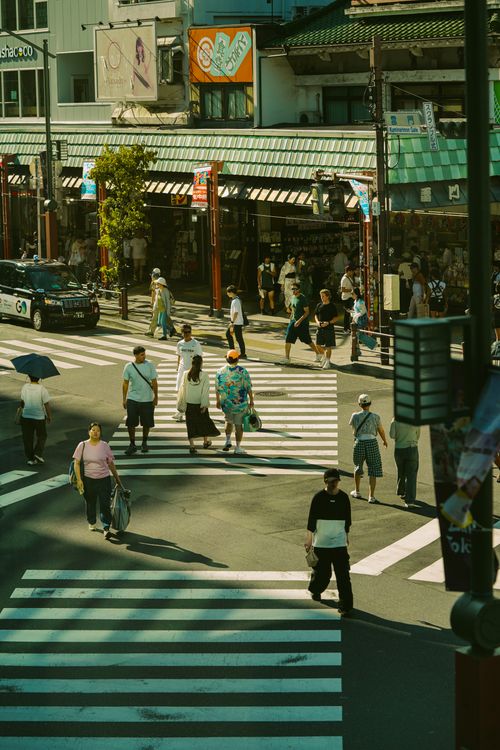 Free Pedestrians crossing a busy street intersection in a bustling urban area on a sunny day. Stock Photo