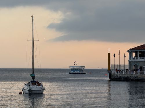 Free A serene scene of a sailboat and ferry near Kadıköy Pier, İstanbul at sunset. Stock Photo