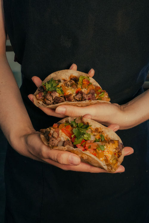 Free Two freshly prepared beef tacos garnished with cilantro and tomatoes in a dimly lit setting. Stock Photo