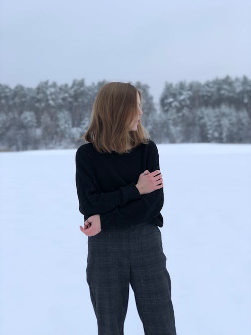 Woman in Black Sweater Standing on Snow Covered Ground