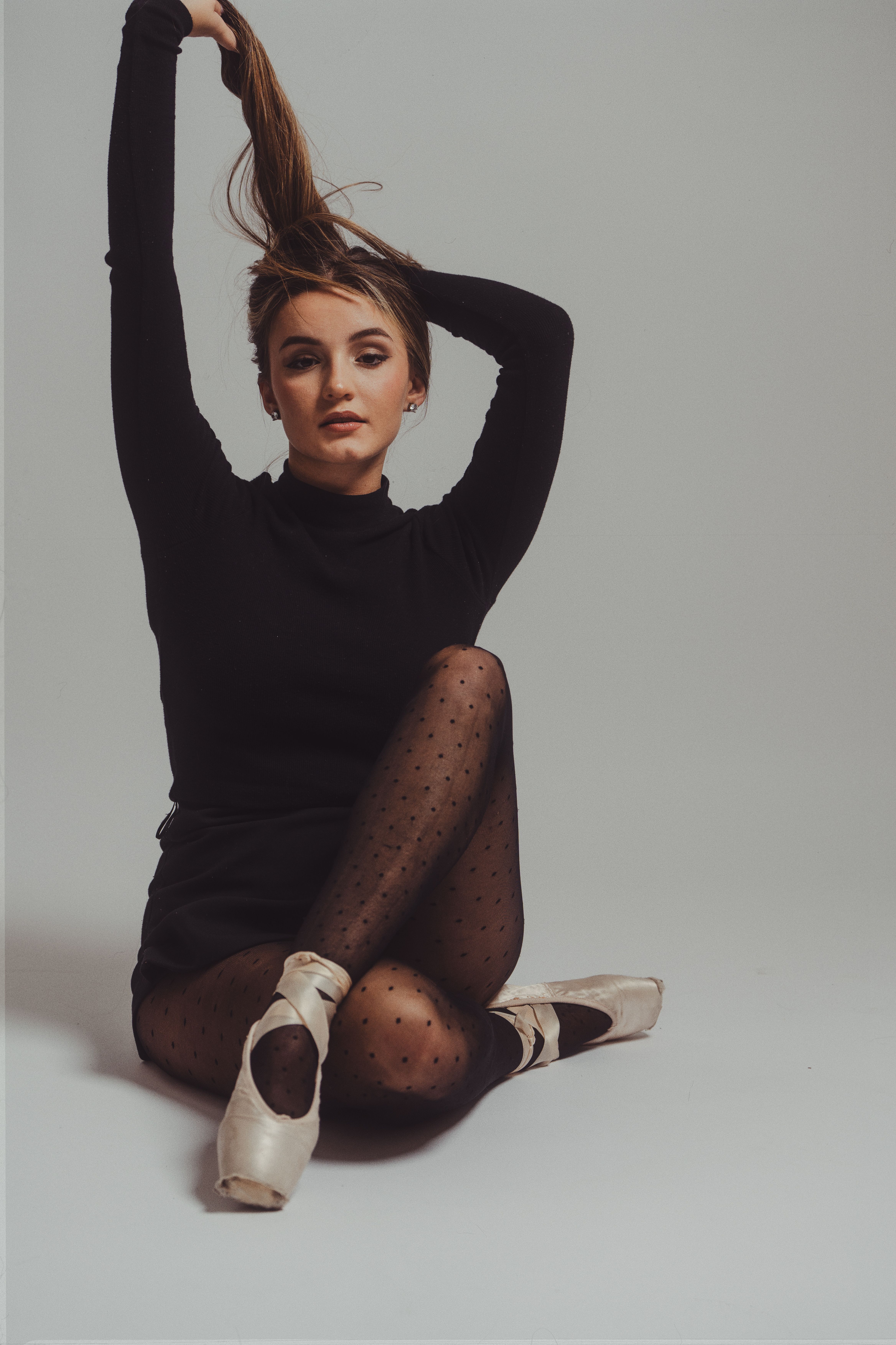 Ballet dancer in black attire and pointe shoes posing gracefully in a studio setting.