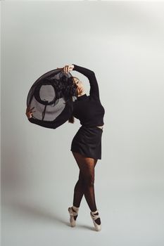 Ballerina elegantly posing on pointe in a studio setting, full body shot with black attire.