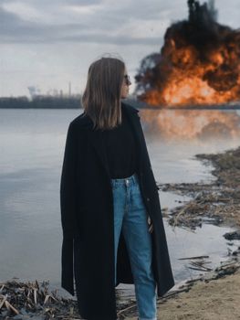 湖边穿着外套的女人，以爆炸为背景，营造出戏剧性的场景