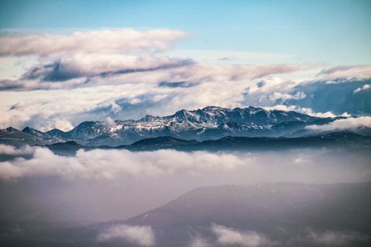 Majestic mountain peaks rise through a layer of clouds under a vibrant blue sky.