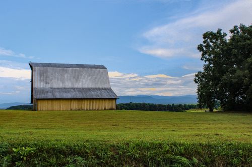 Free Peaceful rural scene with a barn, open field, and mountain backdrop under a clear blue sky. Stock Photo