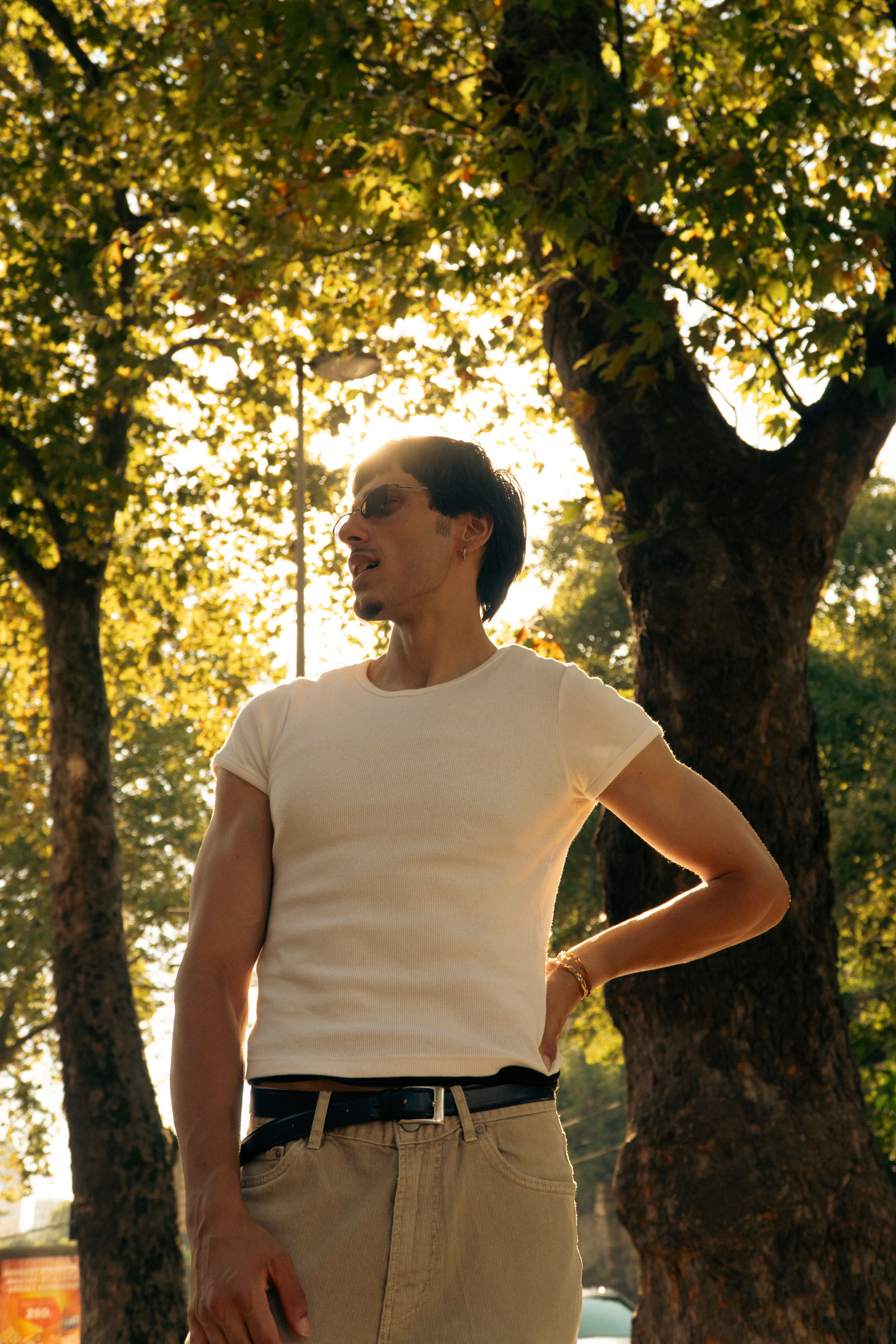 A man in a white shirt stands in an İstanbul park with sunlight filtering through trees.