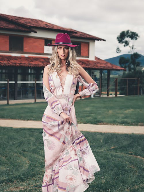 Woman In White And Pink Floral Dress Wearing Red Hat Standing On Green Grass 