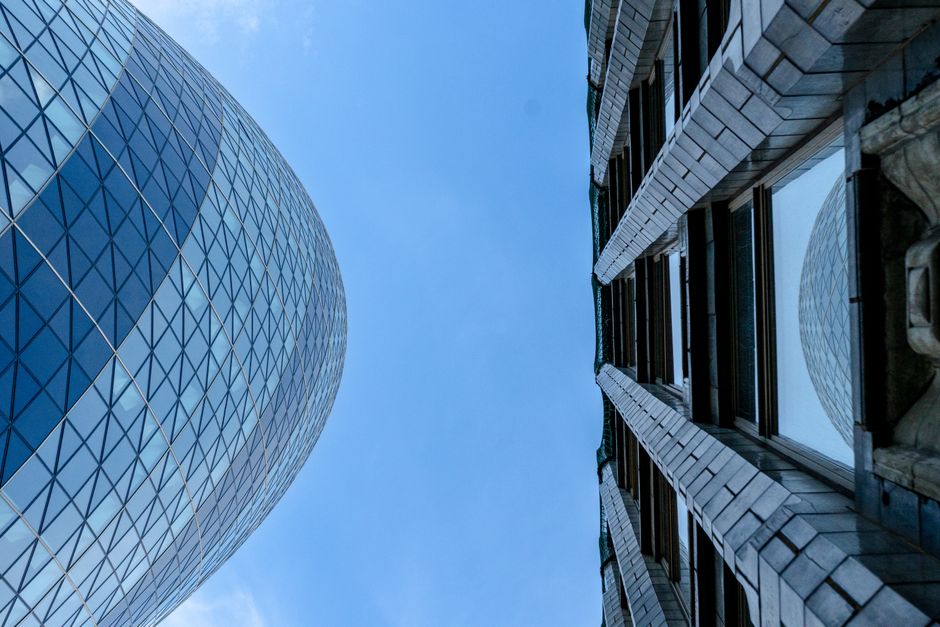 Iconic Gherkin and another building viewed from below against a blue sky in London.