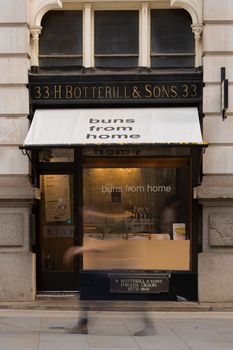 Street view of a London bakery with motion blur of a passerby, evoking urban life.