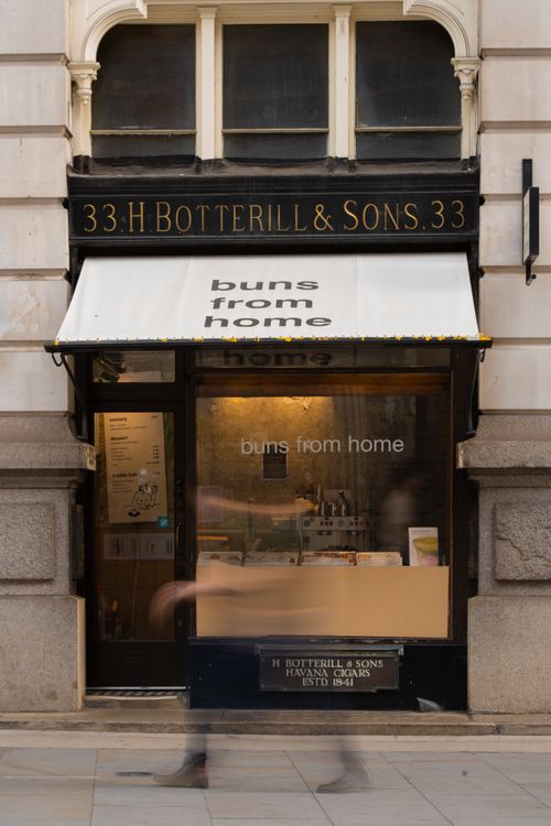 Free Street view of a London bakery with motion blur of a passerby, evoking urban life. Stock Photo