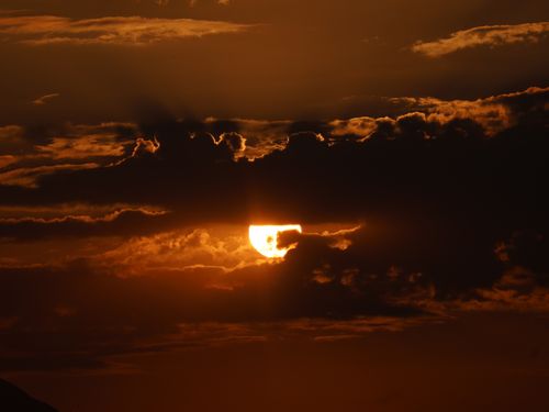 Free Captivating sunset with the sun peeking through dark clouds, creating a dramatic sky. Stock Photo
