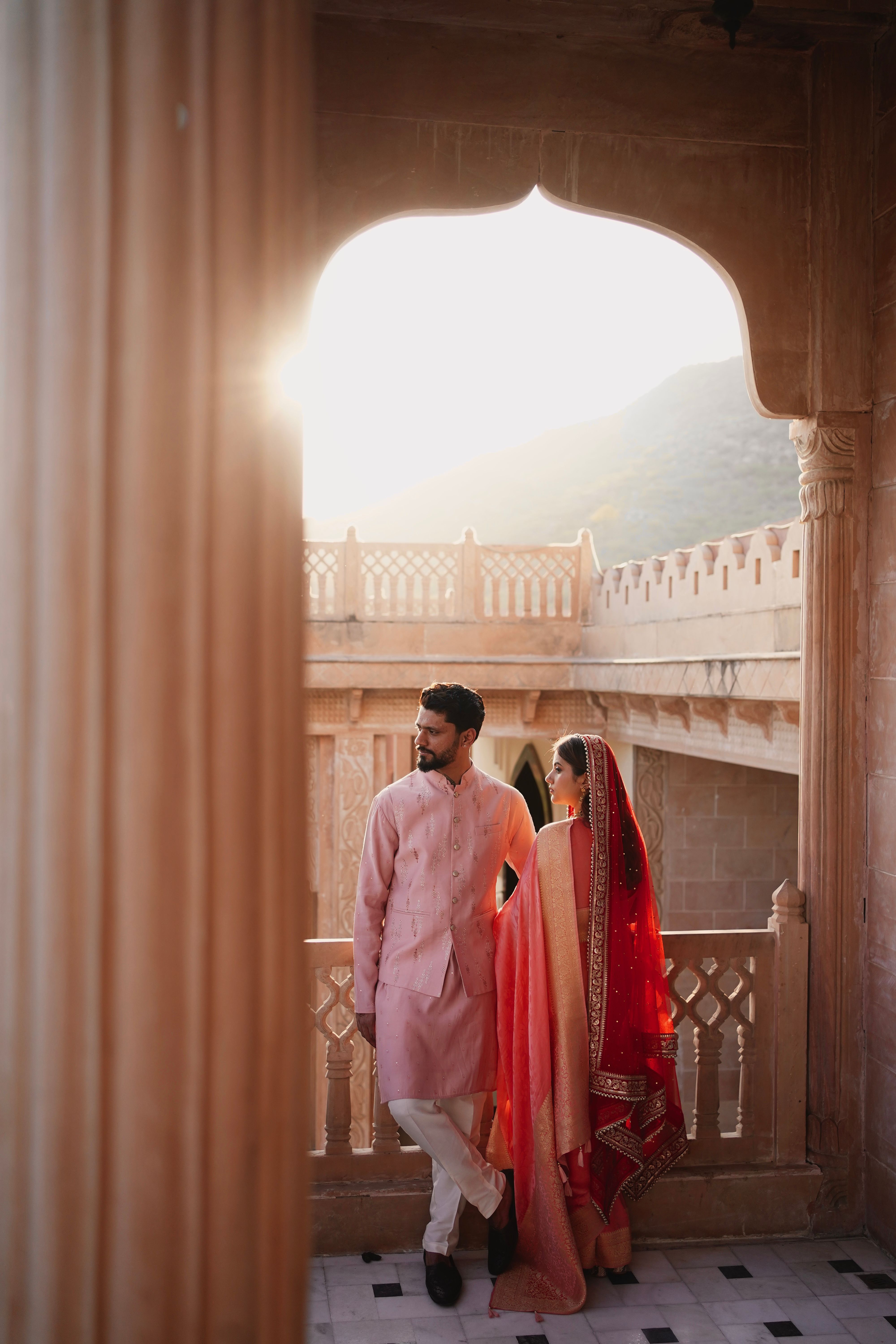 Romantic couple in traditional attire at a palace balcony during sunrise, embracing love and culture.
