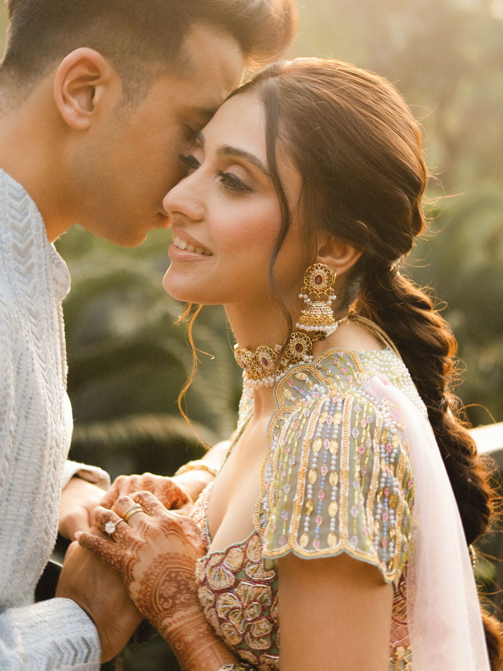 A couple close together in low golden light, her mehndi hand in his.