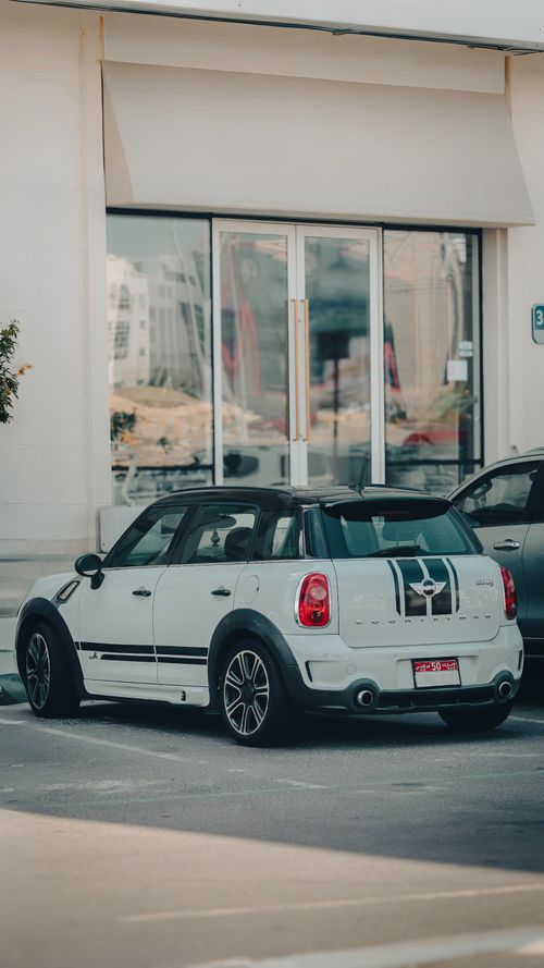 Free White compact car with stripes parked outside a modern glass storefront in UAE. Stock Photo