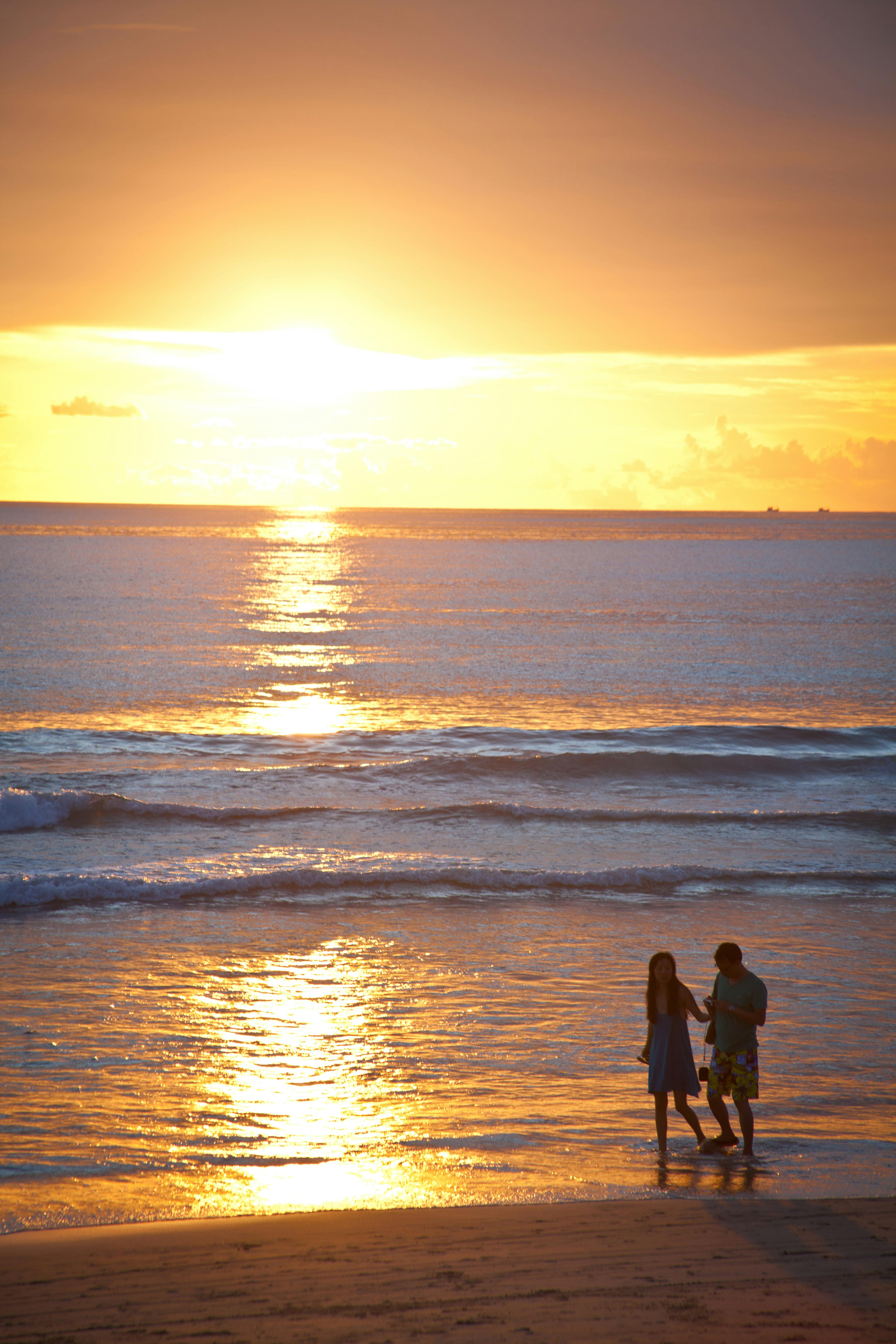 一对夫妇在日落时分沿着海滩宁静地散步，景色令人惊叹