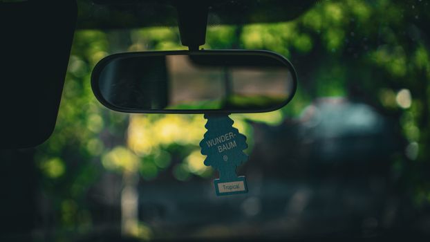 Rearview mirror inside a car with a Wunder-Baum tropical air freshener hanging.