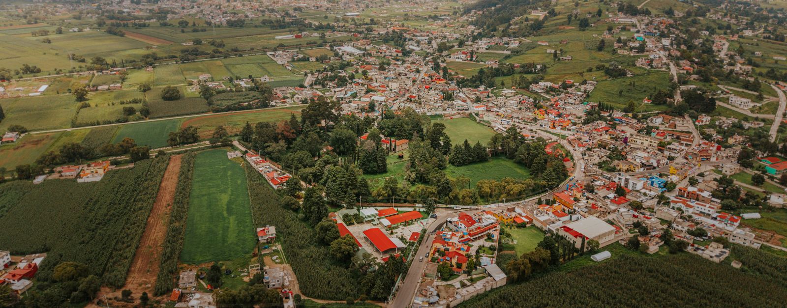Panoramic aerial image of Santiago Tianguistenco with lush green fields and distant mountains.