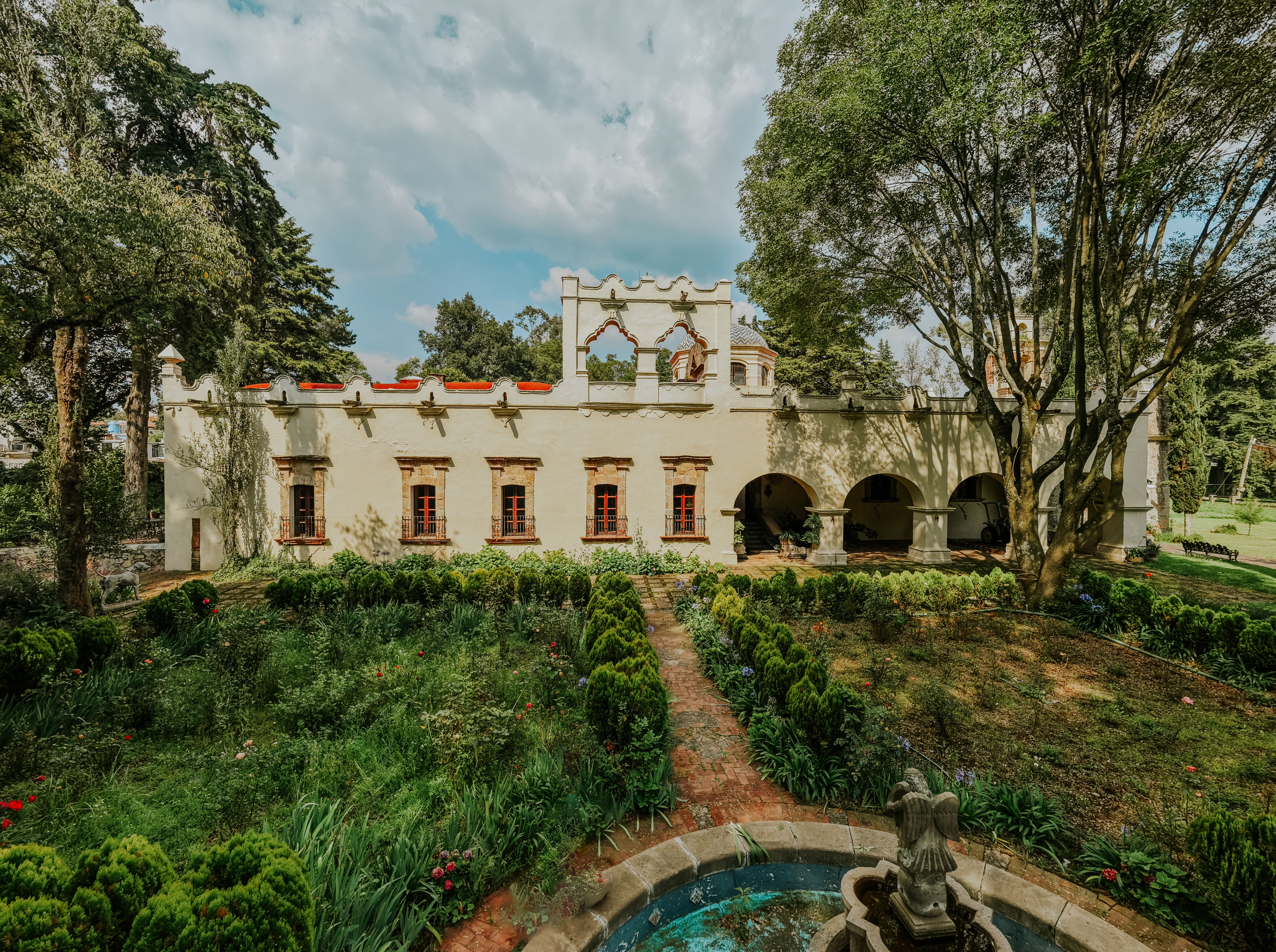 A beautiful historic mansion with a lush garden and fountain, showcasing classic Mexican architecture.